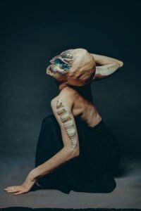 a strange crouching creature with shoulder fins and a blue and gold alien face