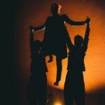 three silhouetted dancers, two dancers lifting the third above their heads by the arms