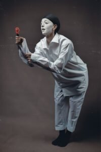 Gillian as Pierrot in a white costume and white painted face holding a rose