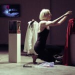Gillian in a blond wig kneeling on the floor