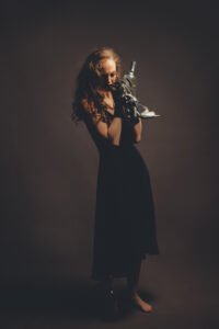 a woman in a black dress carrying her shoes and a bottle of alcohol and crying