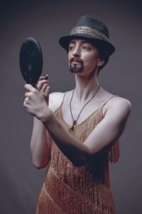 a man wearing a dress and looking into a mirror while applying lipstick